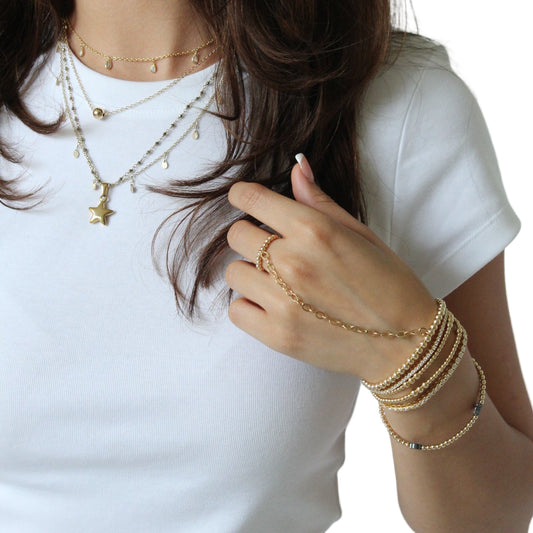 Woman wearing gold jewelry including bracelets and a necklace, with a plain background.